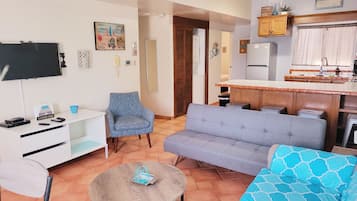 Un salon avec un canapé, un fauteuil, une télévision et une petite table.
