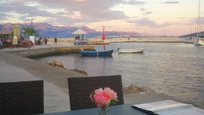 A table with a vase of flowers, overlooking a waterfront with boats and mountains in the background. - Waterfront Dalmatian Stone Villa with Panoramic Adriatic Views, Kastel Novi (Kaštel Novi)