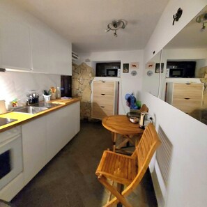 A compact kitchen with white cabinets, a stone accent wall, a microwave, and a small dining table with a chair.
