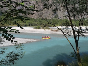 A group of people in a yellow raft on a river surrounded by rocky cliffs and greenery. - LE MAS DES ALBERGES. (Le Bourg-D'oisans)