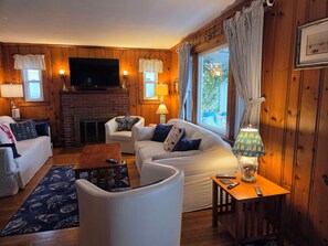 A cozy living room with a fireplace, a television, and a comfortable seating area with a sofa and armchairs. - Adorable Cottage, short walk to Beach Weekly and Monthly offering until May 2026 (Narragansett)