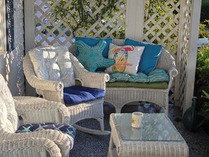 A wicker outdoor seating area with a cushioned bench and chairs, a glass table, and a decorative mug. - Adorable Cottage, short walk to Beach Weekly and Monthly offering until May 2026 (Narragansett)