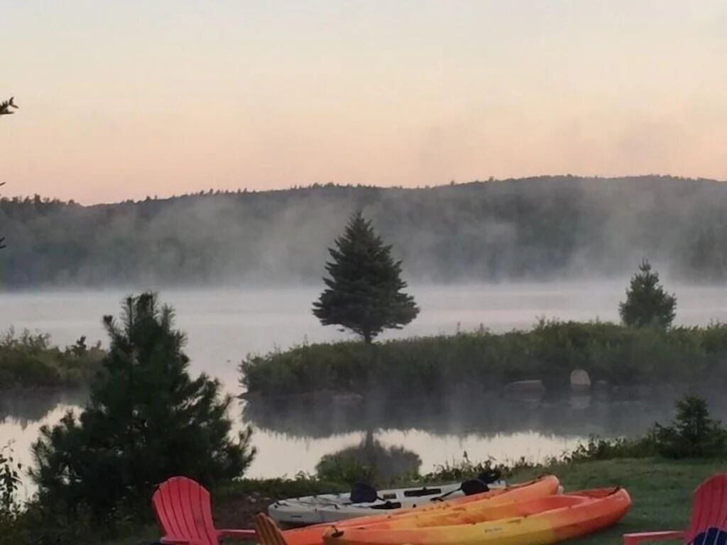 Un paysage paisible au bord d’un lac, avec des kayaks et des chaises Adirondack rouges.