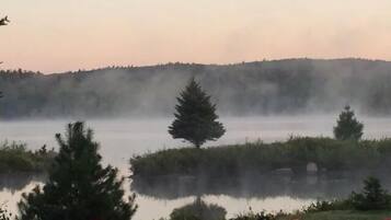 Un paysage paisible au bord d’un lac, avec des kayaks et des chaises Adirondack rouges.