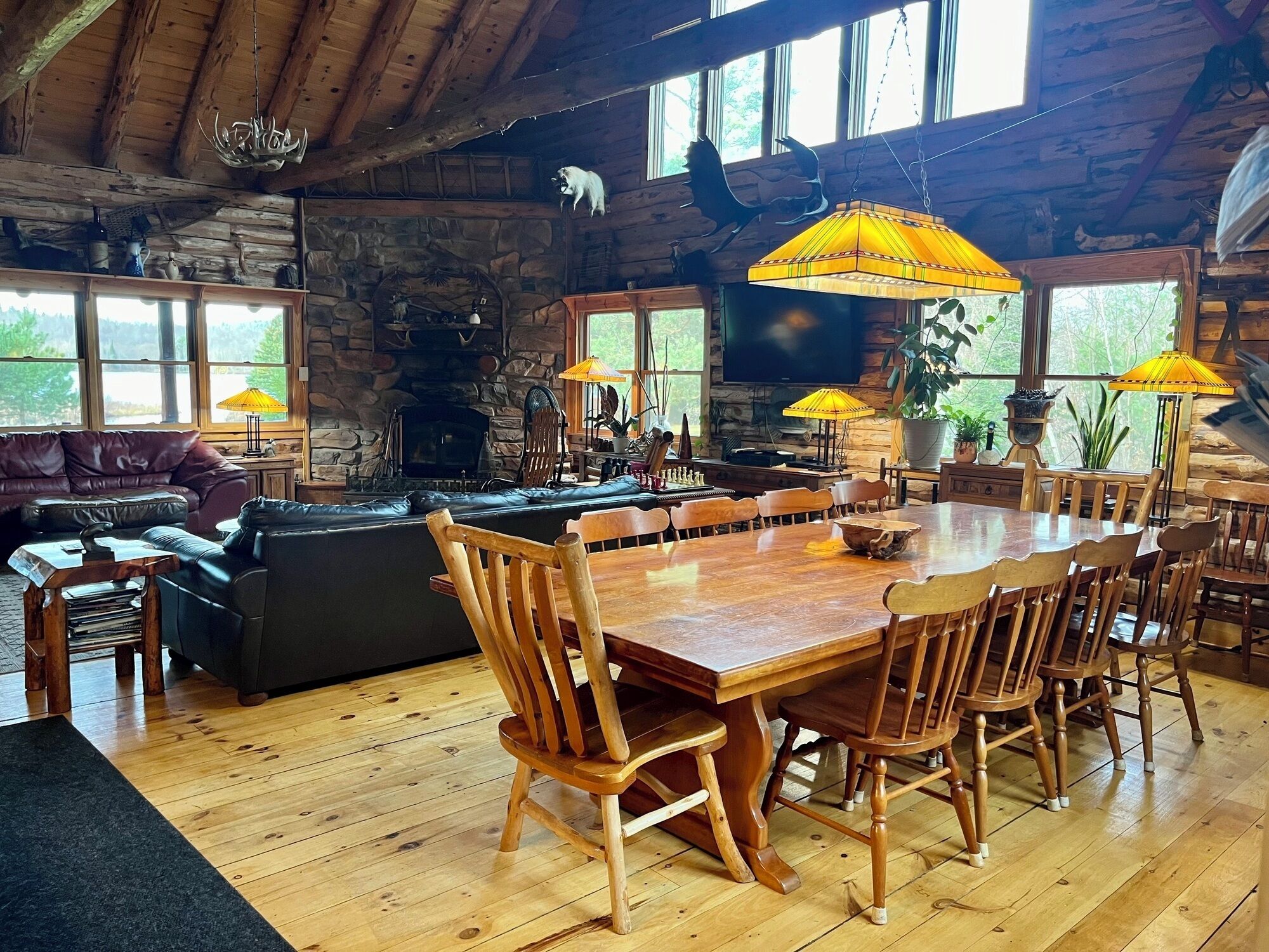 A rustic cabin interior with a stone fireplace, wooden dining table, and comfortable seating.