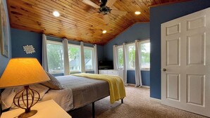 A bedroom with a bed, a nightstand, a lamp, a ceiling fan, and a door. - Beautiful lakefront, family-friendly! (Hustisford)