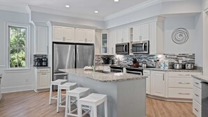 Una cocina moderna con armarios blancos, electrodomésticos de acero inoxidable y una isla central con taburetes de bar.