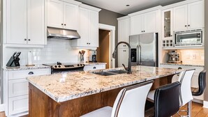 A modern kitchen with white cabinetry, a granite countertop, stainless steel appliances, and a central island with bar stools.