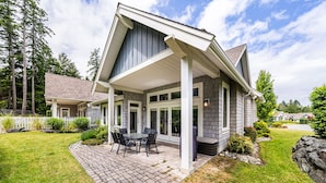 A modern house with a covered patio, a brick pathway, and a white picket fence.
