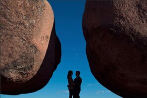 A couple standing between two large rock formations with a clear blue sky in the background.
