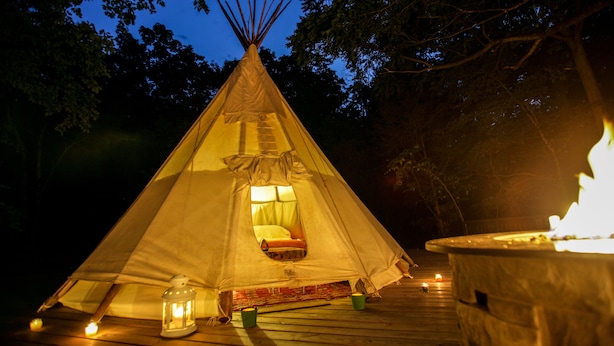 A teepee with a bed inside, a lantern, and a fire pit on a wooden deck at night. - ❤️ THE MAGIC TIPI RETREAT (Park Hills)