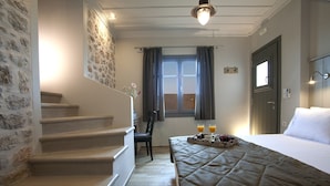 Ein Hotelzimmer mit einem Bett, einem Nachttisch mit zwei Gläsern Orangensaft, einem Fenster mit Vorhängen, einer Treppe und einer Steinwand.