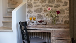 Ein rustikaler Holztisch mit einer Steinwand im Hintergrund, ein Stuhl, eine Vase mit Blumen und eine Obstschale mit zwei Gläsern Orangensaft.