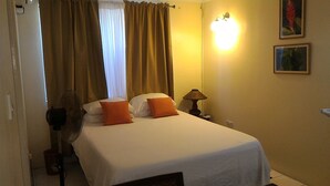 A hotel room with a bed, curtains, a nightstand with a lamp, and a wall-mounted light. - Rodney Bay Beach Home near EVERYTHING (Rodney Bay)