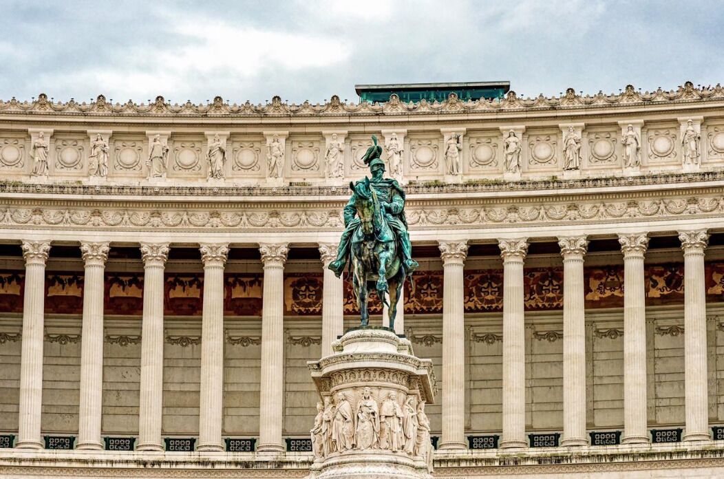 A classical building facade with a central statue on a pedestal, flanked by columns and ornate architectural details.