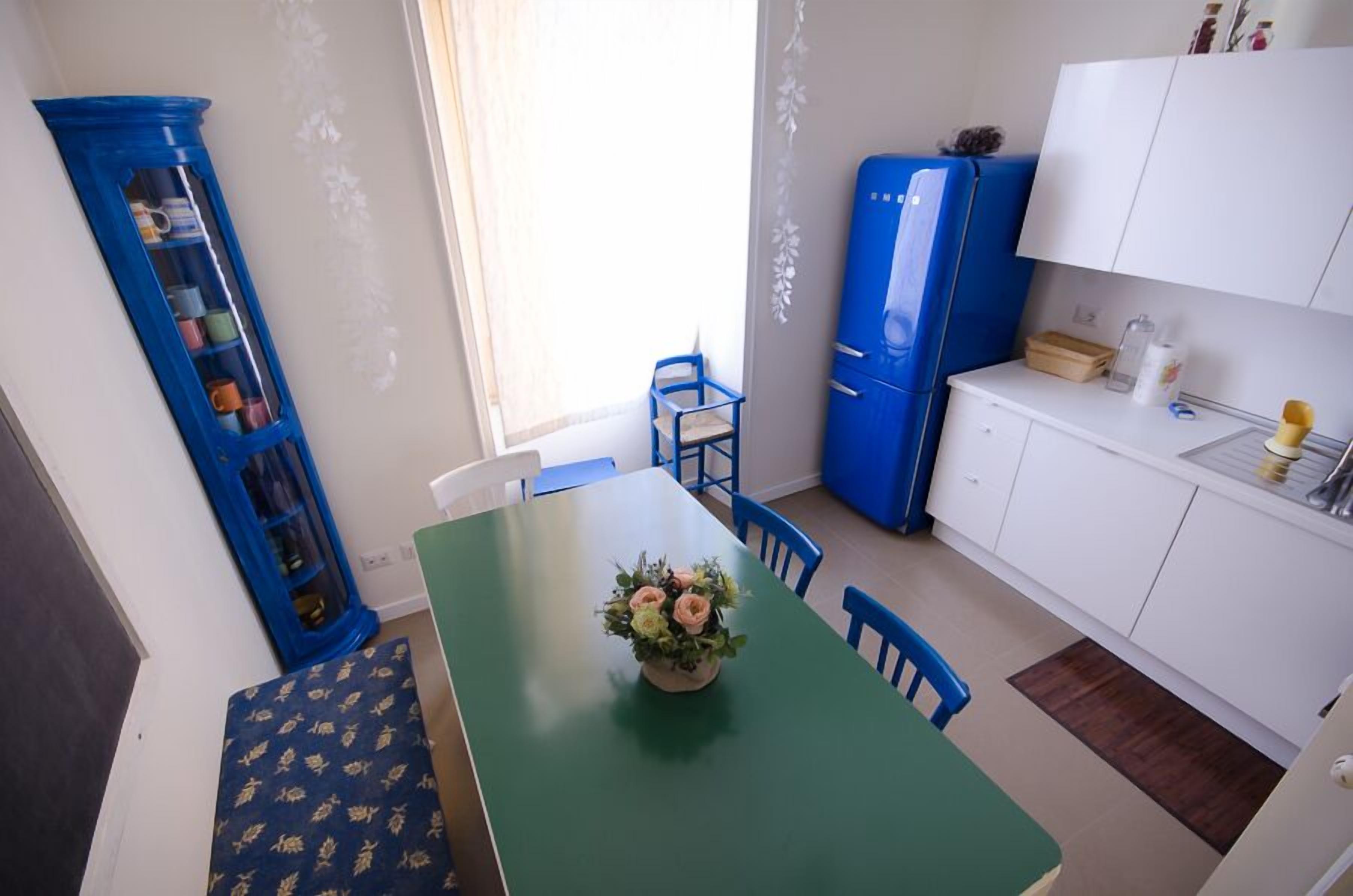 A compact kitchen with a green table, blue chairs, a blue refrigerator, and a white cabinet.