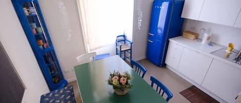 A compact kitchen with a green table, blue chairs, a blue refrigerator, and a white cabinet.
