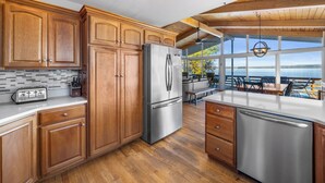 Una cocina moderna con armarios de madera, electrodomésticos de acero inoxidable y vistas al océano a través de amplias ventanas.