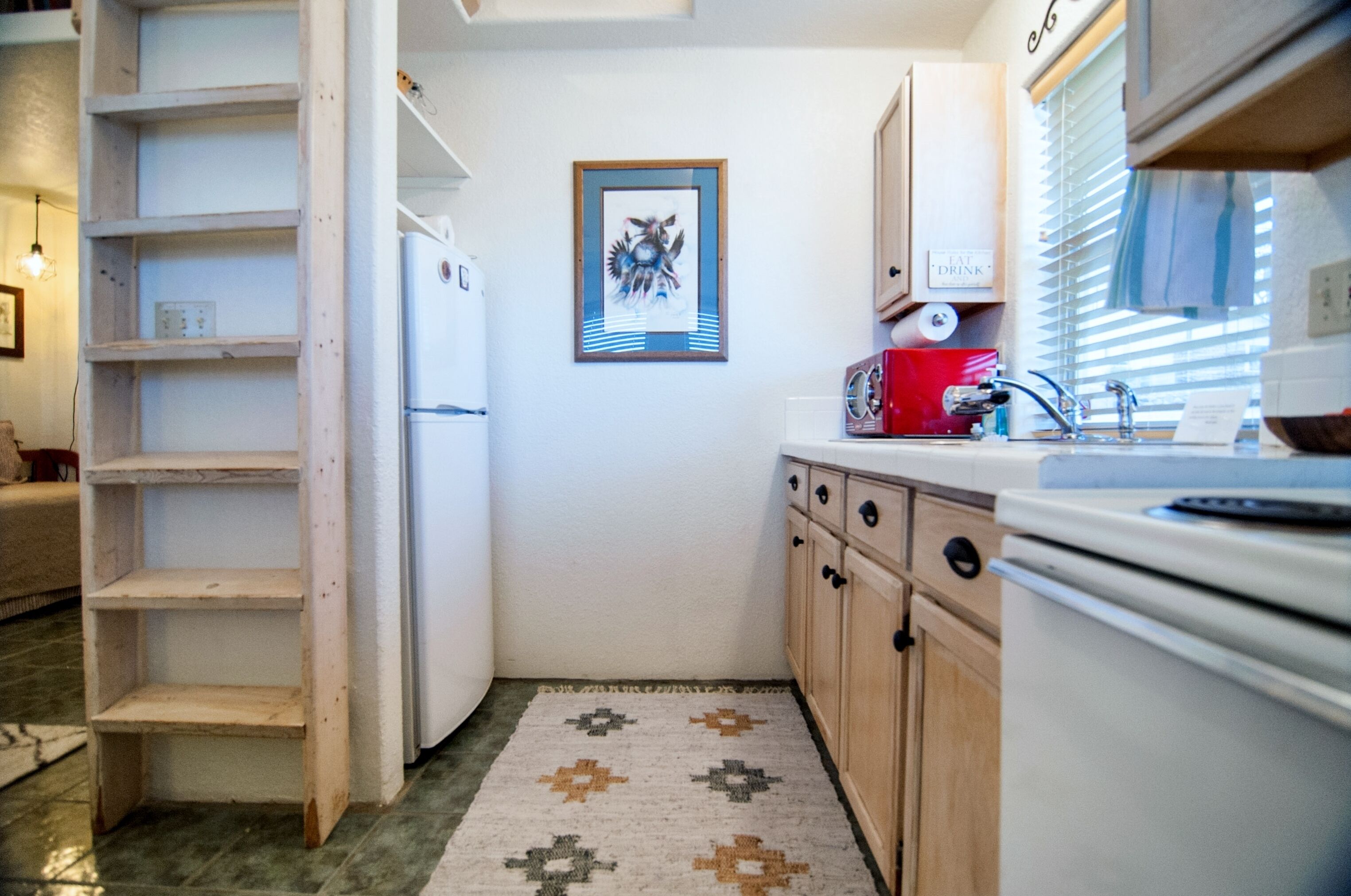 Una cocina compacta con armarios blancos, un refrigerador, un lavabo y una alfombra estampada.