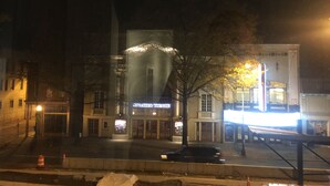 A building with a marquee sign, a street with a car, and a tree.
