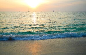 A beach with waves and a sunset in the background.
