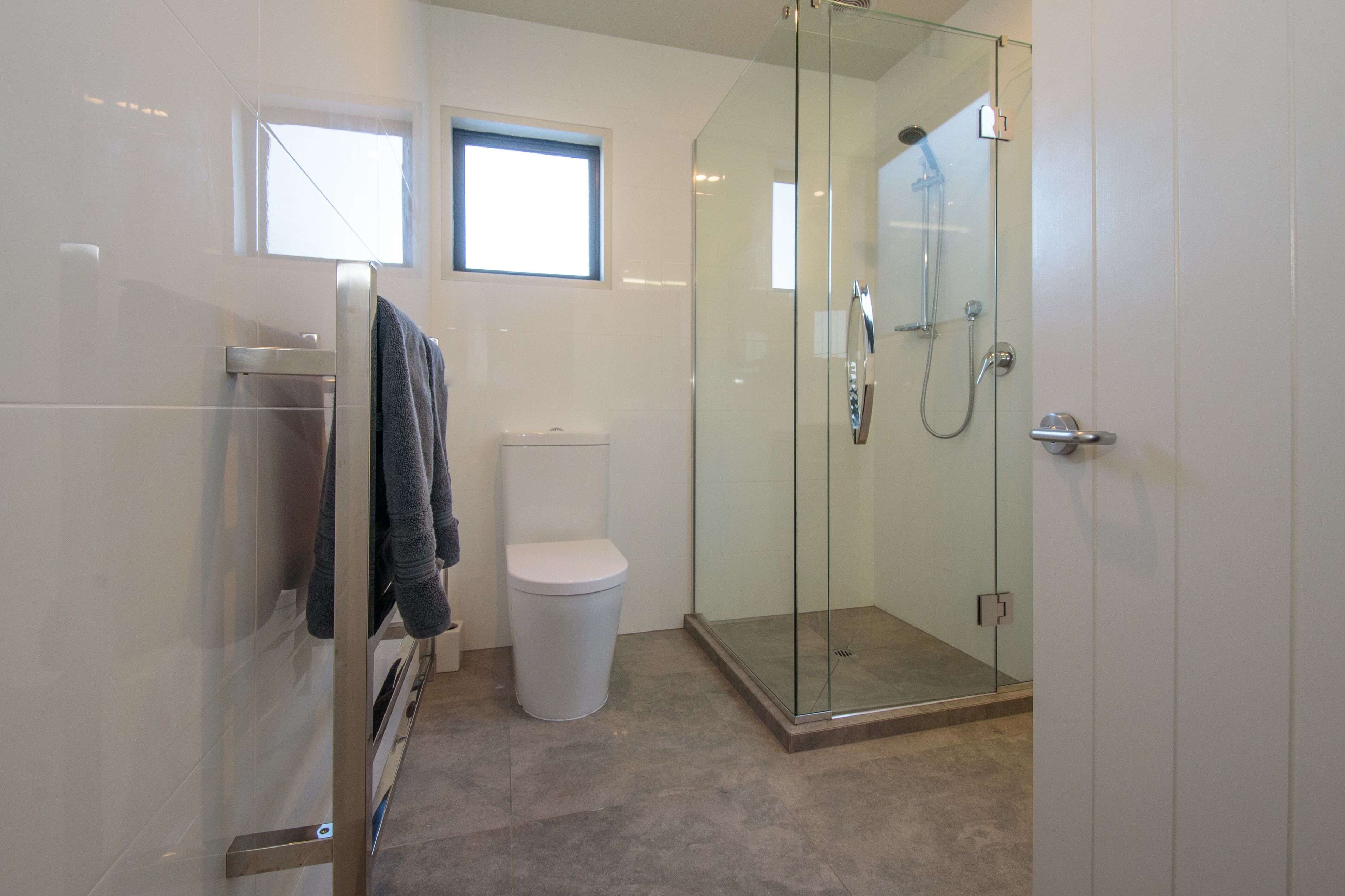 A modern bathroom with a glass-enclosed shower, a toilet, and a towel rack.