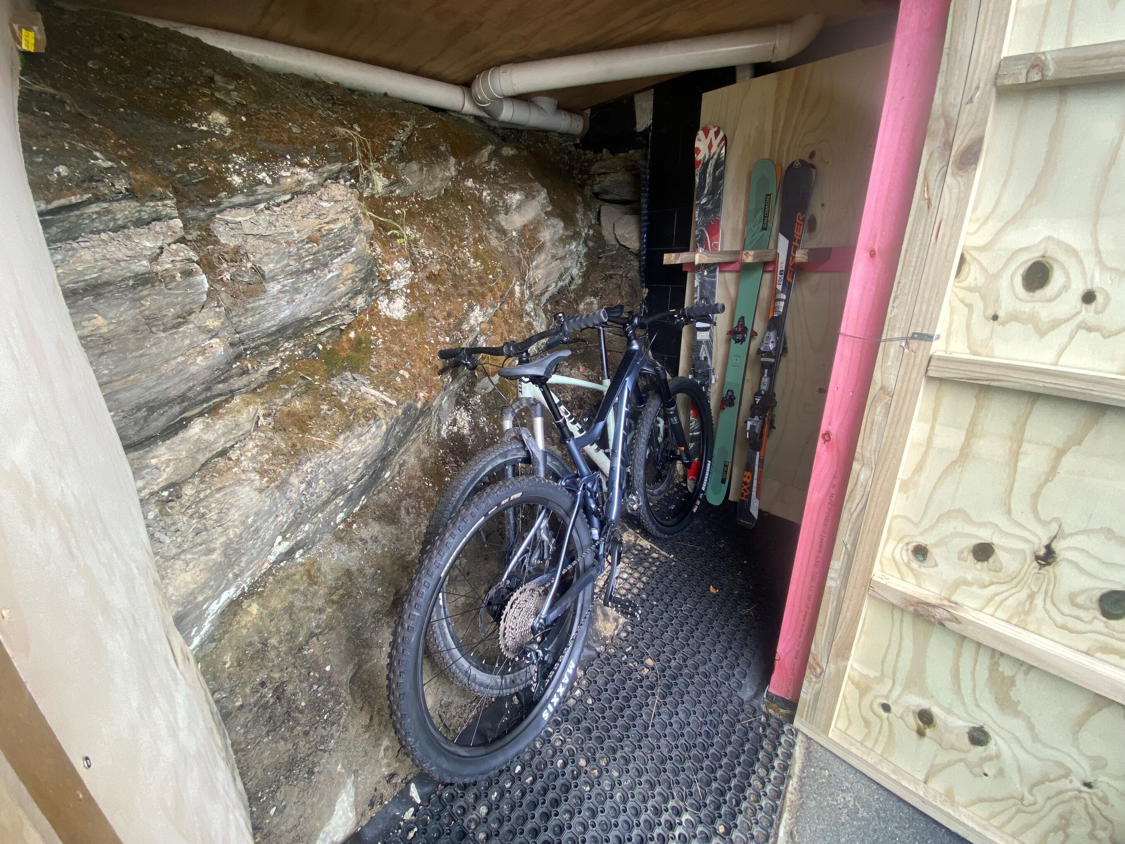 Een mountainbike en ski's opgeborgen in een houten constructie met een rotsachtige muur.