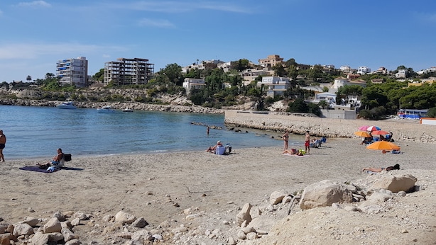 A beach with rocky terrain, people sunbathing, and boats in the water. - Front Line Apartment south facing with Pool, next to Sea, new fibre internet. (El Campello)