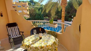 A balcony with a table, chairs, a bottle of wine, and a view of a swimming pool and greenery. - Front Line Apartment south facing with Pool, next to Sea, new fibre internet. (El Campello)