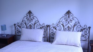 A double bed with a metal headboard, a bedside table with a lamp, and a plain wall. - Holiday home - Casa Ruà (Zoagli)