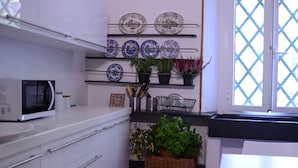 A kitchen with white cabinets, a microwave, and shelves with plates and potted plants. - Holiday home - Casa Ruà (Zoagli)