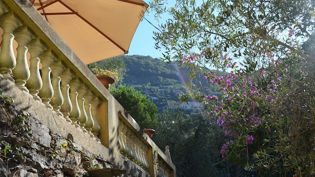 A stone balustrade with a beige umbrella, a view of a hillside with buildings, and flowering shrubs. - Holiday home - Casa Ruà (Zoagli)