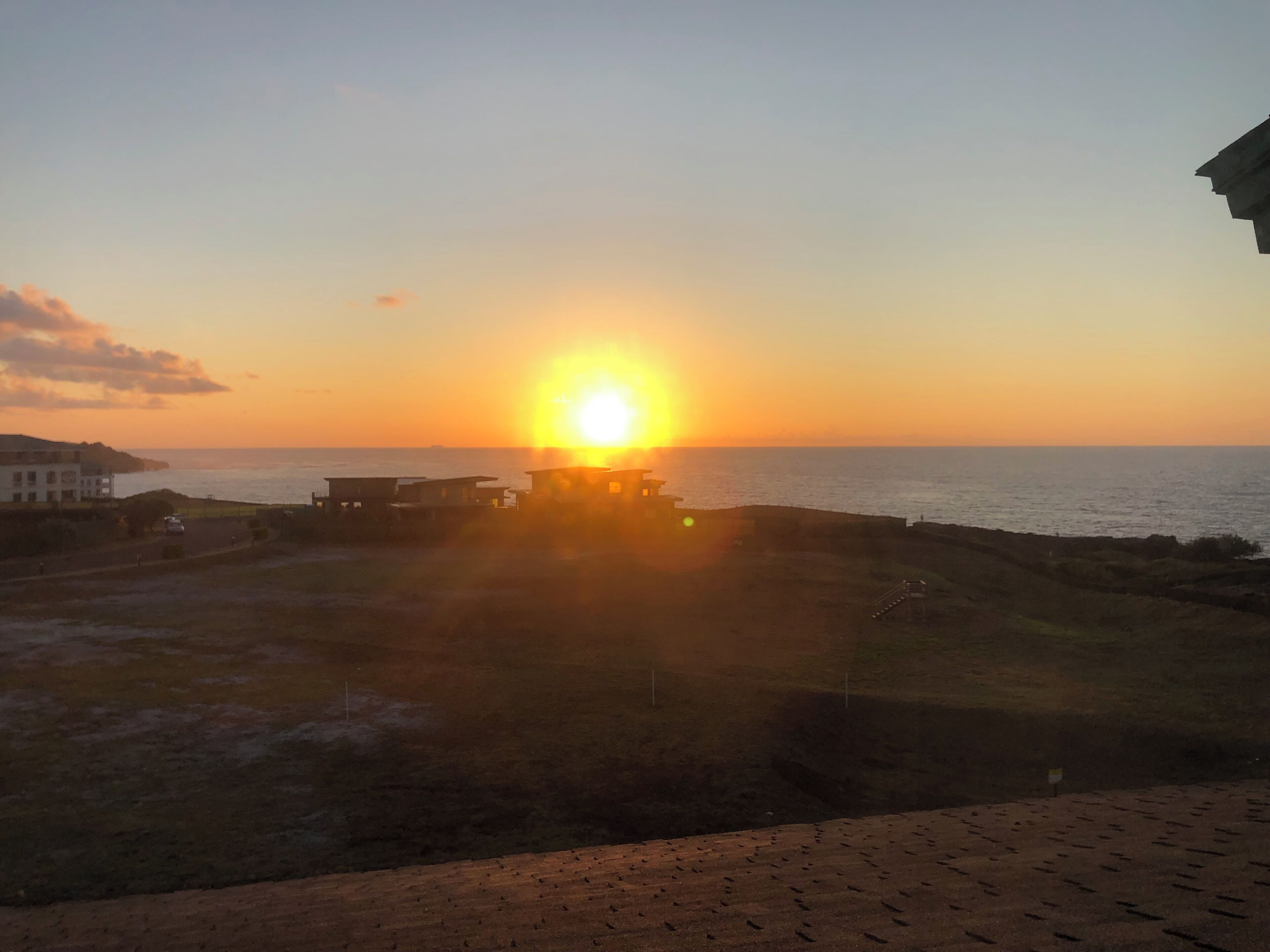 A sunset over a coastal area with buildings and a clear sky.