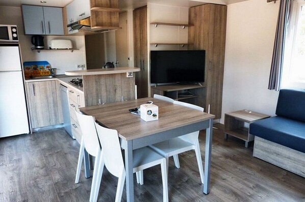 A compact kitchenette with a microwave, coffee maker, and a small refrigerator. There is a dining table with chairs and a television in the corner.