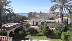 A coastal residential area with a white building, palm trees, and a view of the sea.
