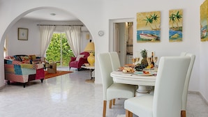 A spacious living room with a dining area, featuring a colorful sofa, a red armchair, and a white dining table with chairs.
