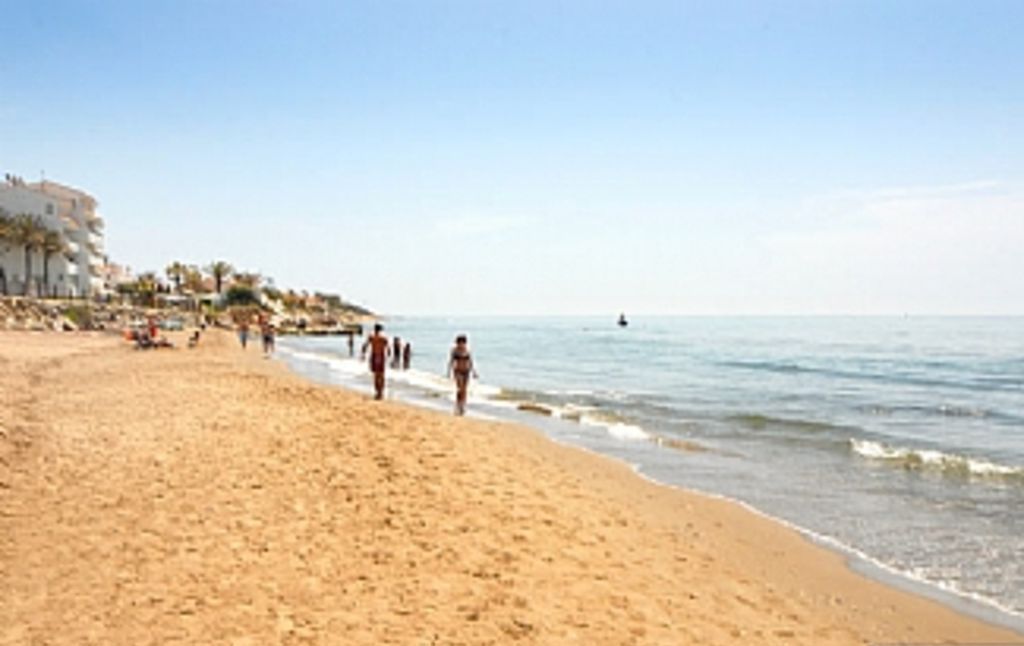 A sandy beach with people walking along the shore.