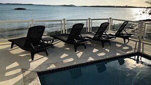 Zona junto a la piscina con sillones de descanso y vista al océano.