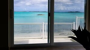 Vista a través de un ventanal hacia un balcón con vista a aguas turquesas y una isla distante.