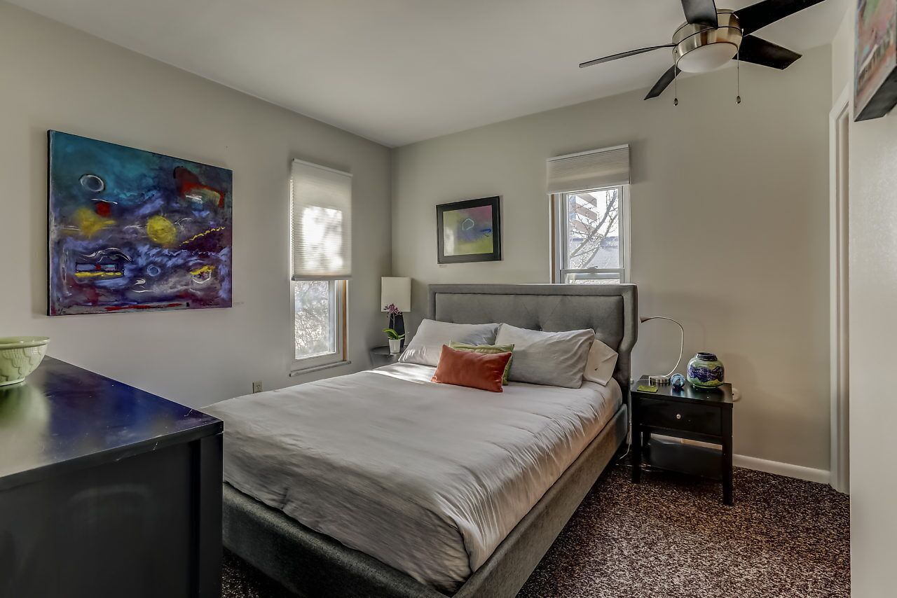 Ein Schlafzimmer mit Bett, Deckenventilator, Nachttisch und einem Bild an der Wand.