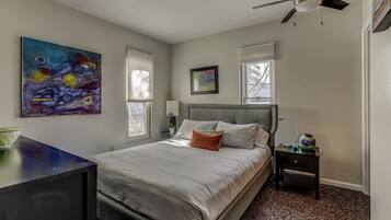 Ein Schlafzimmer mit Bett, Deckenventilator, Nachttisch und einem Bild an der Wand.
