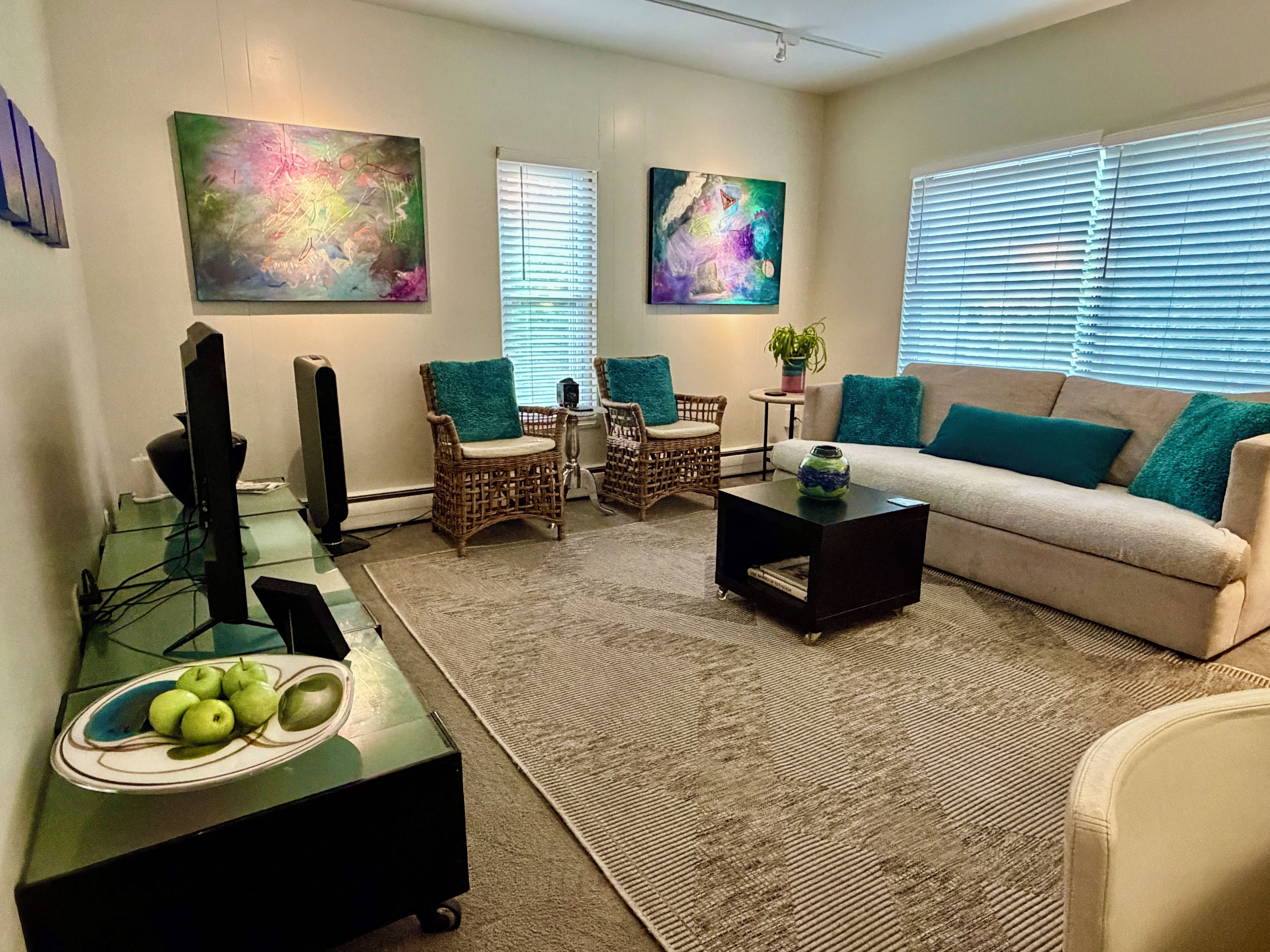 A living room with a sofa, two chairs, a coffee table, and artwork on the walls.