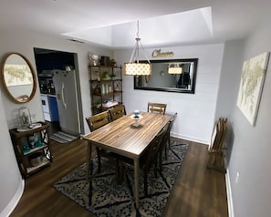 Een eetgedeelte met een houten tafel en stoelen, een kroonluchter, een boekenkast en een spiegel aan de muur.