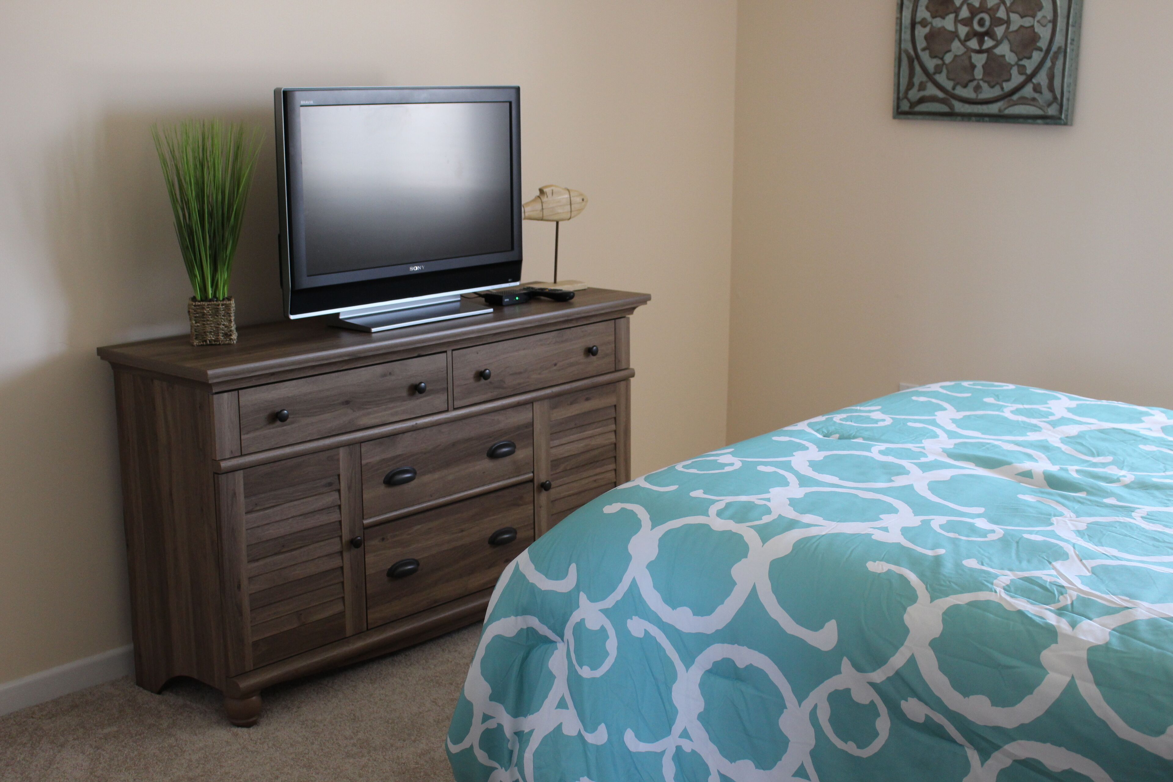 A bedroom with a bed, a dresser, a television, and a wall decoration.