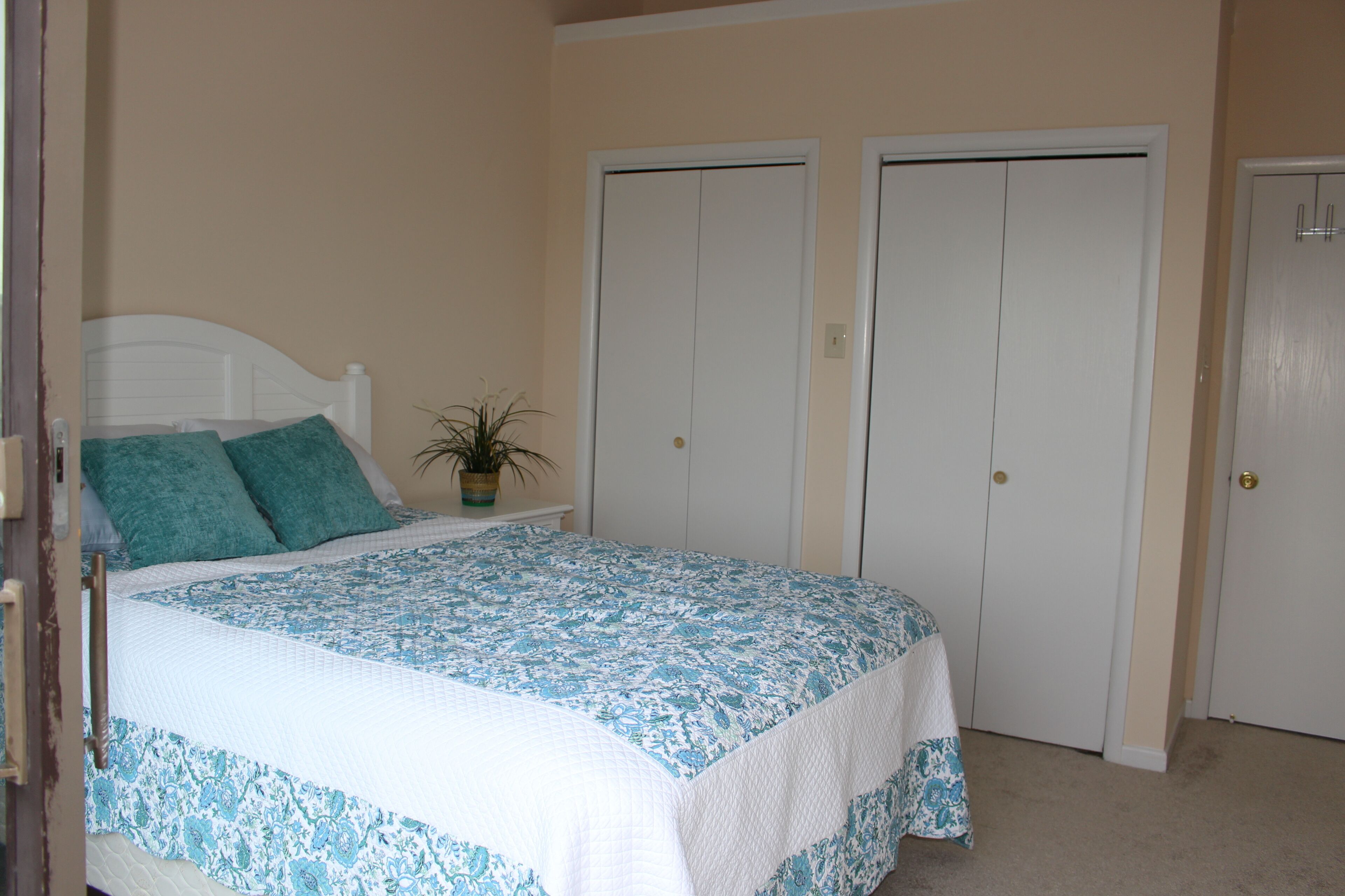 A bedroom with a bed, two white doors, and a potted plant.