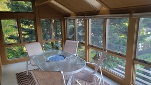 Ein Wintergarten mit Glastisch und -stühlen, großen Fenstern und Blick auf einen Wald.