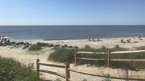 Ein sandiger Strand mit einem Holzzaun im Vordergrund, einem klaren blauen Himmel und einem ruhigen Meer.