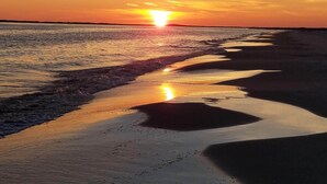 Une plage au coucher du soleil, où le soleil se reflète sur le sable mouillé.