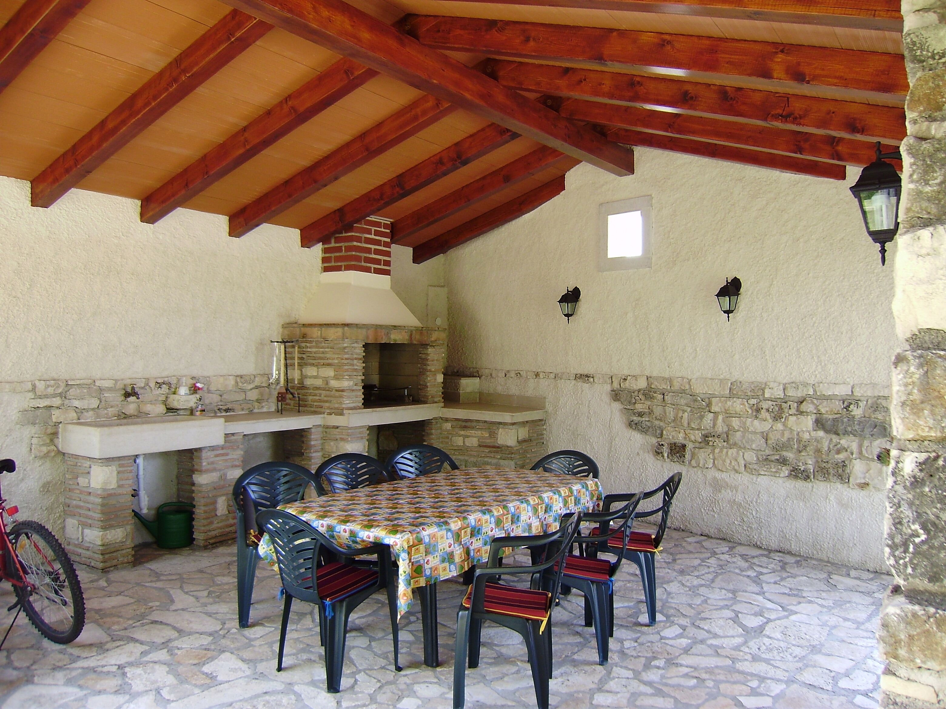 An outdoor patio with a stone fireplace, a table with chairs, and a bicycle.