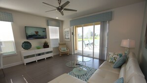 A modern living room with a white sofa, glass coffee table, and a ceiling fan. - Outstanding, owner operated Townhome,  even a TV in the pool area! (Clermont)